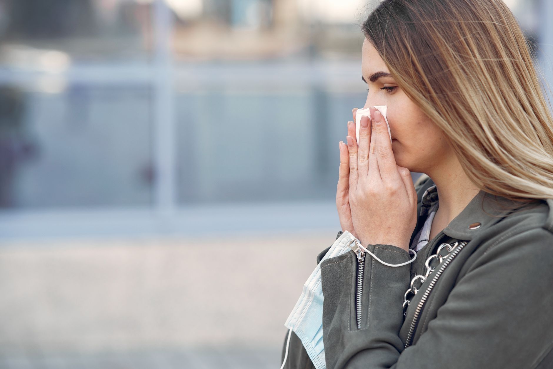 A woman outdoors holding a tissue to her nose on a bright day during hay fever season